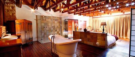 Una habitación amplia con una bañera grande, suelo de madera y una pared de piedra.