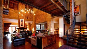 A spacious living area with a fireplace, leather sofas, a wooden coffee table, and a chandelier. - Afrique Boutique Hotel Ruimsig (Roodepoort)