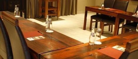 A conference room with a long wooden table, chairs, a projector screen, and a small table with a vase of flowers.