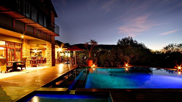 A pool area with a wooden deck and a stone building in the background. - Afrique Boutique Hotel Ruimsig (Roodepoort)