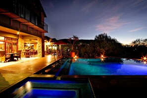 A pool area with a wooden deck and a stone building in the background. - Afrique Boutique Hotel Ruimsig (Roodepoort)