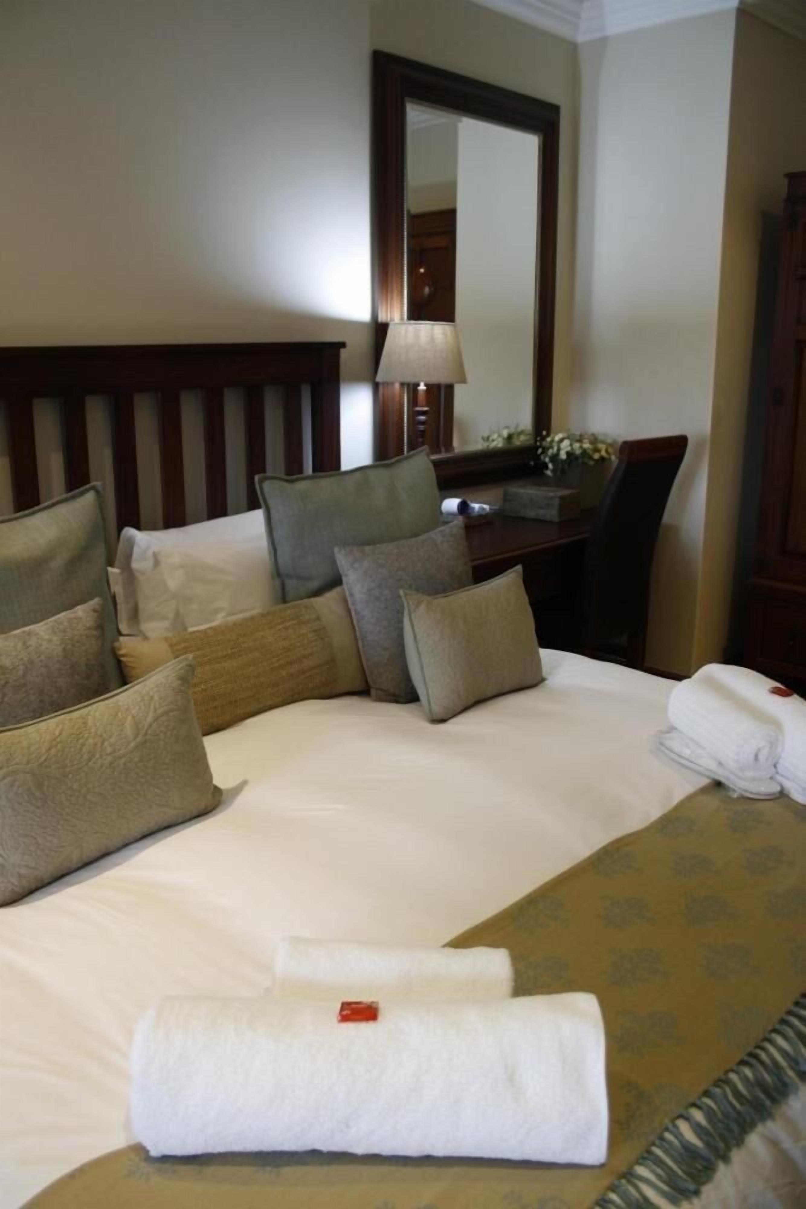 A hotel room with a neatly made bed, a desk with a lamp, and a mirror on the wall.