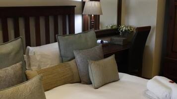 A hotel room with a neatly made bed, a desk with a lamp, and a mirror on the wall.