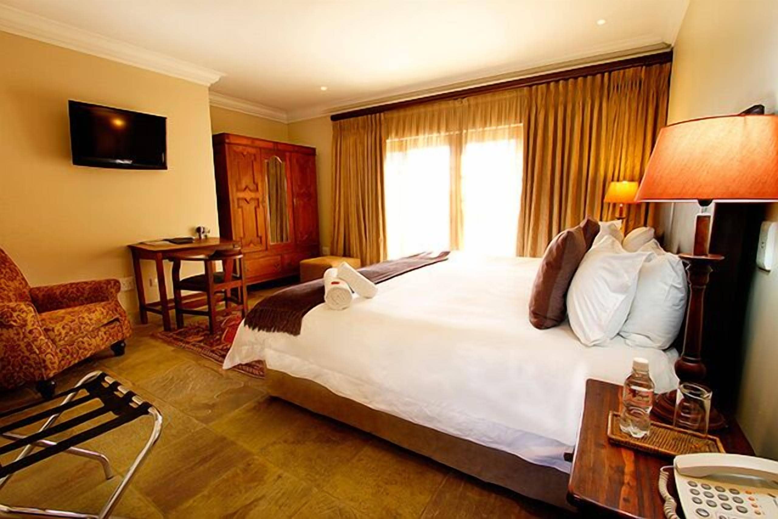Een hotelkamer met een groot bed, een televisie, een bureau, een stoel en een raam met gordijnen.