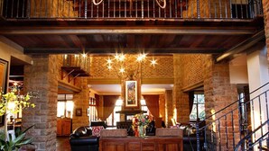A spacious lobby with a wooden staircase, a chandelier, and a patterned rug. - Afrique Boutique Hotel Ruimsig (Roodepoort)