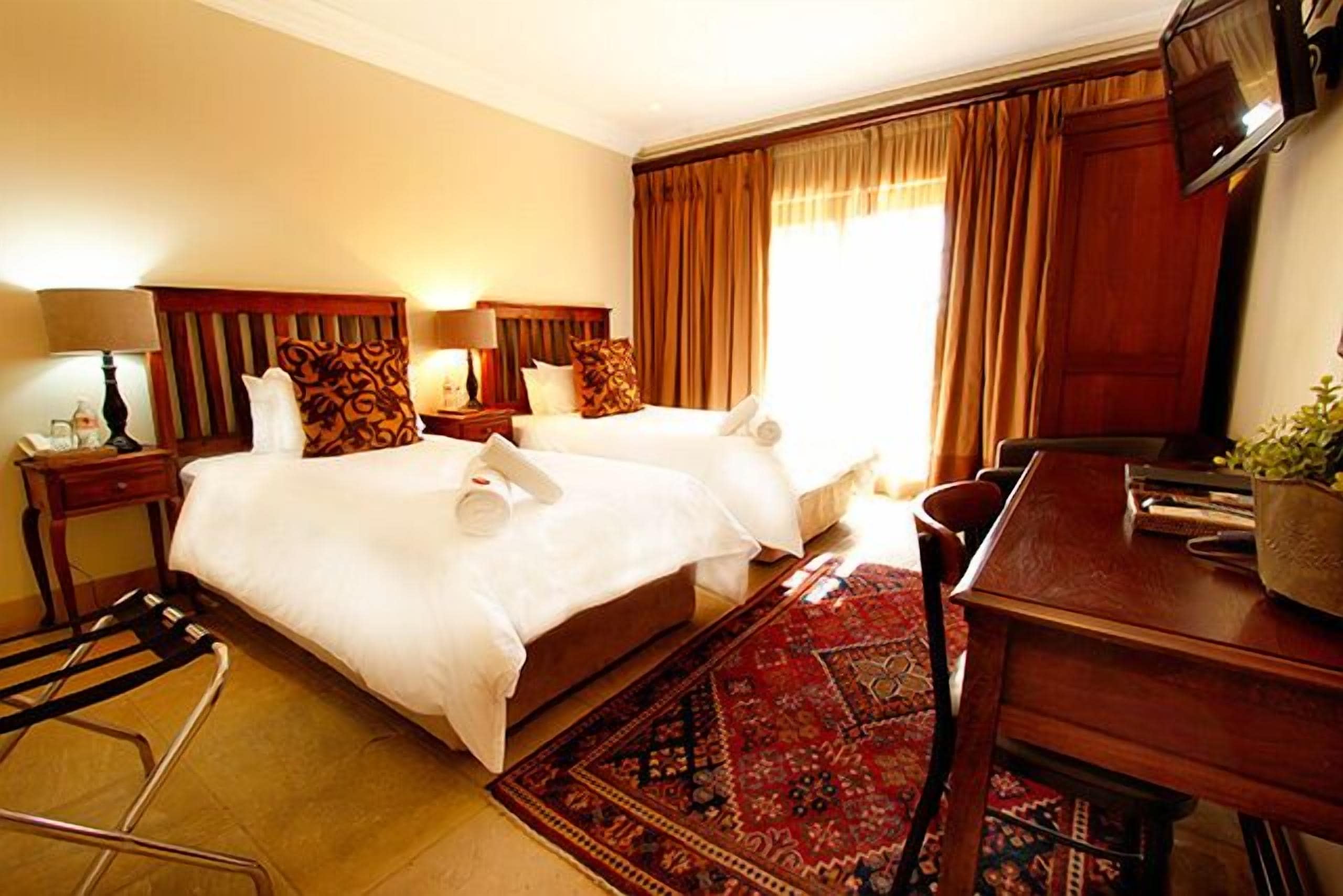 A hotel room with two beds, a desk, a chair, a TV, and a large window with curtains.