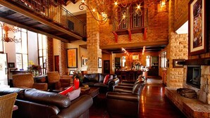 A spacious living room with leather sofas, a fireplace, and a high ceiling with exposed brick walls. - Afrique Boutique Hotel Ruimsig (Roodepoort)