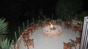 A circular outdoor seating area with a fire pit at the center, surrounded by wooden chairs.