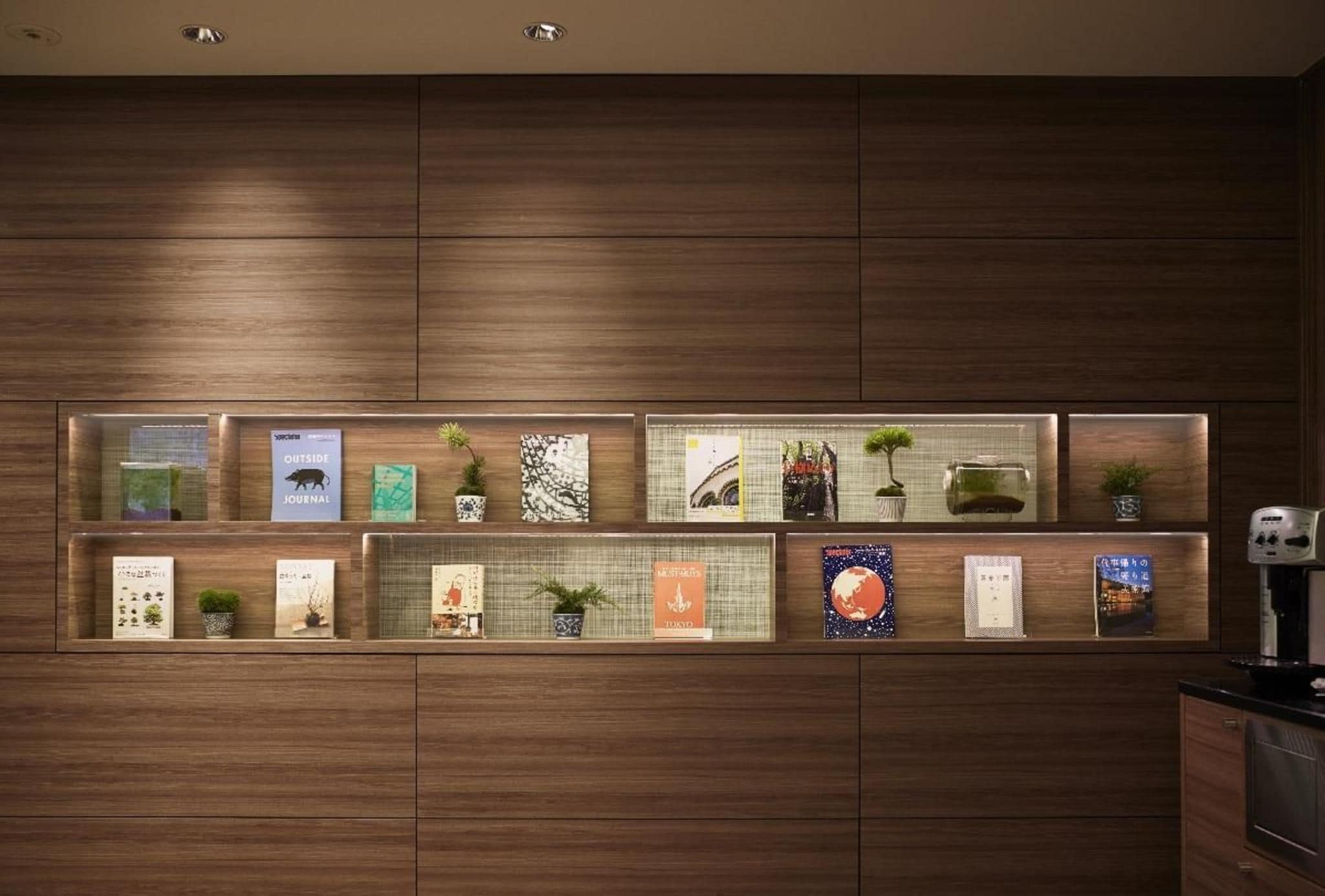 A wall with multiple shelves displaying books and small potted plants.