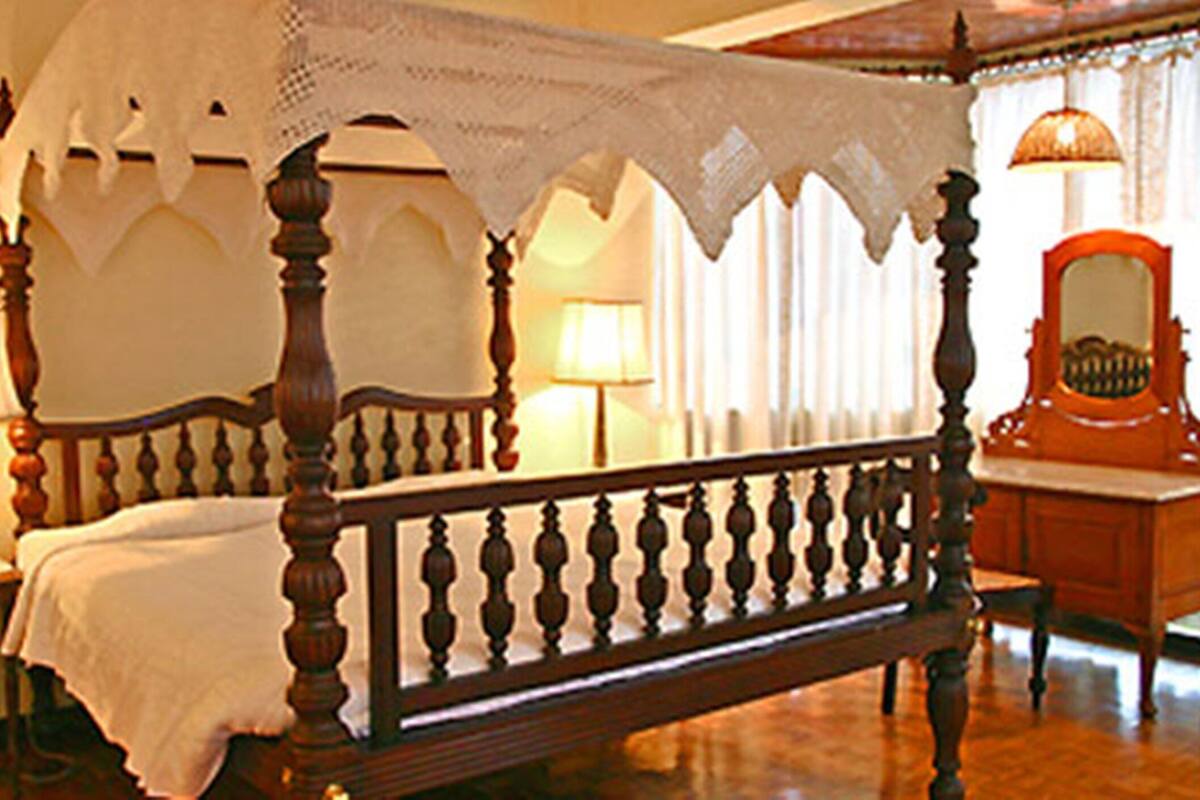 A four-poster bed with a canopy, two bedside tables, a mirror, and a lamp on each side.