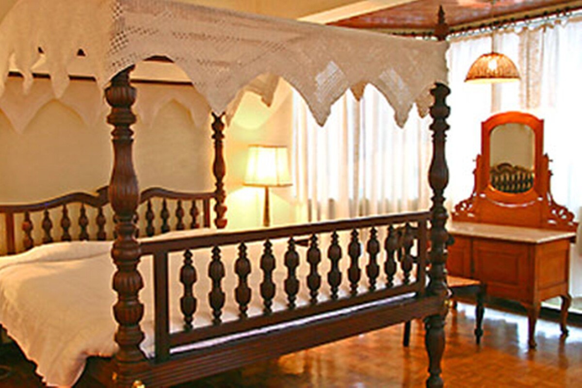A four-poster bed with a canopy, two bedside tables, a mirror, and a lamp on each side.