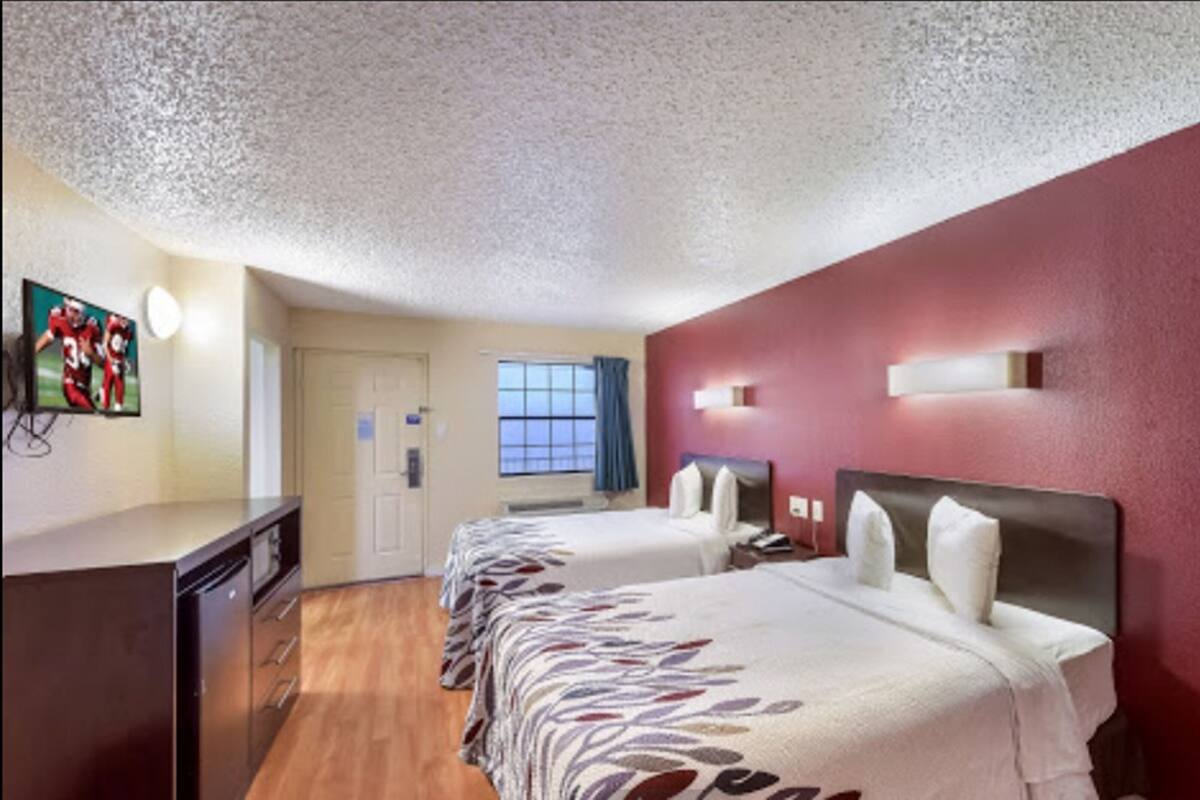 A hotel room with two beds, a TV, a desk, and a window with curtains.