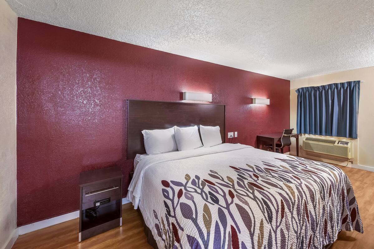 Habitación de hotel con una cama grande, una mesita de noche, un escritorio y un calentador en la pared.