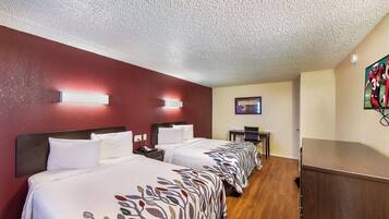 A hotel room with two beds, a desk, a chair, a TV, and a painting on the wall.