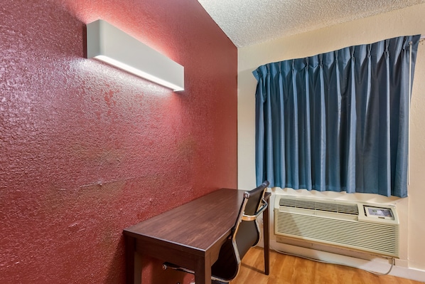 Une pièce avec une table en bois, une chaise, un climatiseur fixé au mur et une fenêtre avec des rideaux bleus.