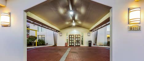 Entrada de un hotel con un vestíbulo techado, una puerta con paneles de vidrio y un letrero con el número de la dirección.