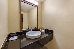 Une salle de bain avec un lavabo blanc, un plan de toilette noir et un grand miroir.