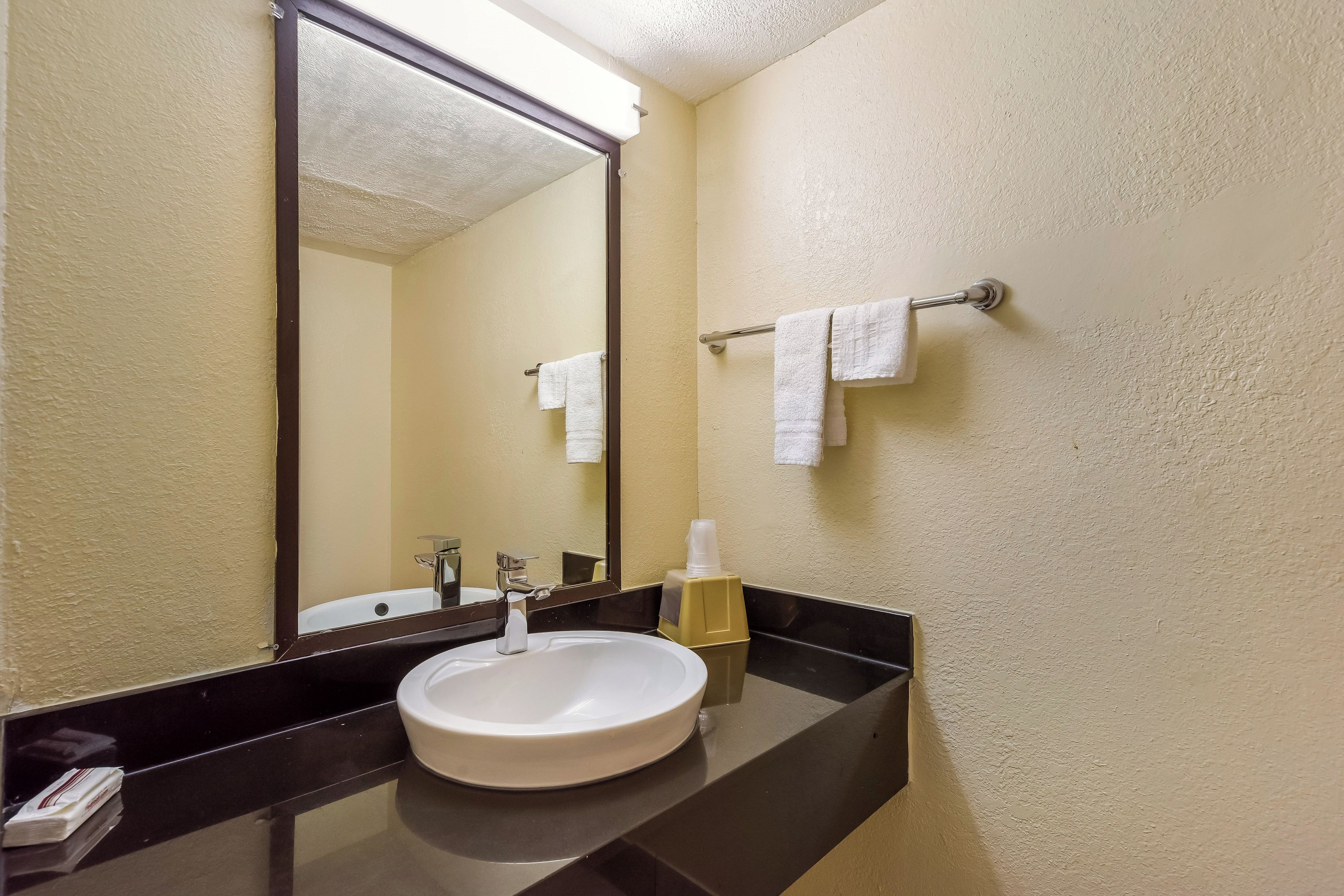 A bathroom with a white sink, a mirror, and a towel rack with two white towels.