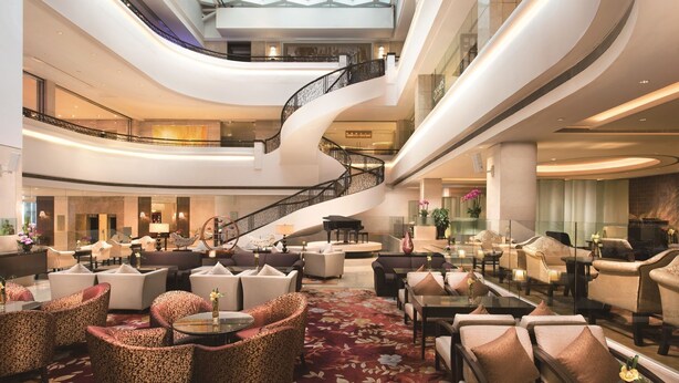 A spacious lobby with multiple seating areas, a grand piano, and a curved staircase. - Shangri-la Hotel (Shenzhen)