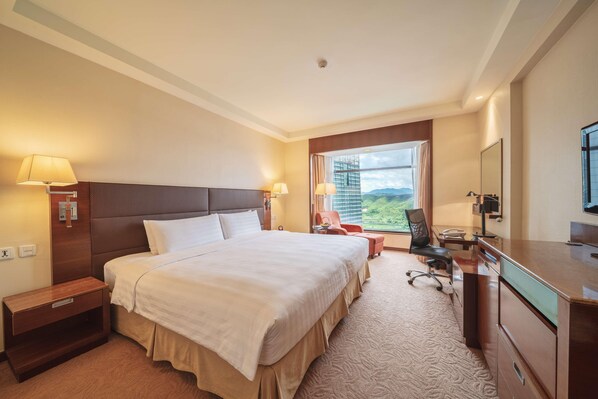 A hotel room with a large bed, a desk with a chair, a TV, and a window with a view of the outdoors. - Shangri-la Hotel (Shenzhen)