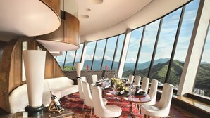 A dining area with a table set for six, surrounded by white chairs, with a view of mountains through large windows. - Shangri-la Hotel (Shenzhen)
