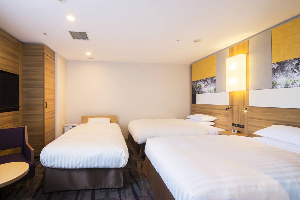 Habitación de hotel con dos camas, un televisor de pantalla plana, una silla y una obra de arte colgada en la pared.