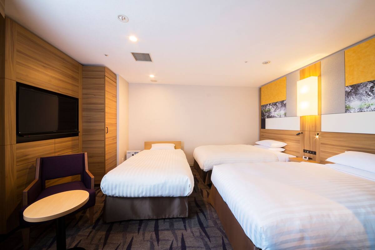 Habitación de hotel con dos camas, televisión, una silla y una mesita.