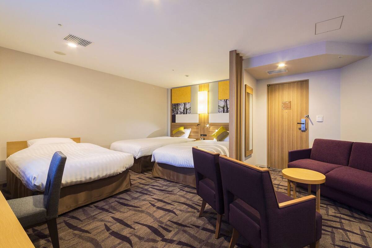 Habitación de hotel con dos camas, un sofá, una mesita y una silla.