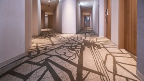 Passadís d'hotel amb una moqueta estampada, parets de tons neutres i portes que donen a les habitacions.