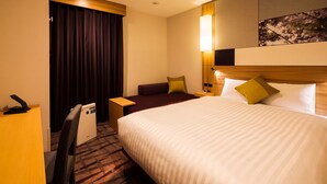 Habitació d'hotel amb un llit gran, escriptori, cadira, tauleta de nit i làmpada penjada a la paret.