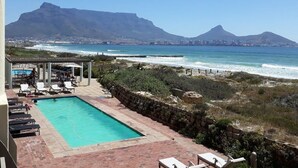 A pool area with lounge chairs, a view of the ocean, and mountains in the background. - Leisure Bay (Cape Town)