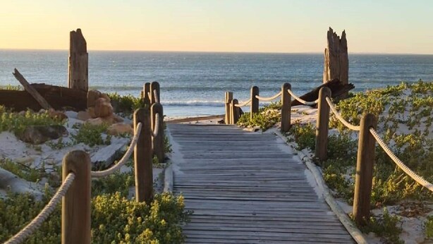 A wooden boardwalk leading to the beach with rope barriers and rocky formations. - Leisure Bay (Cape Town)