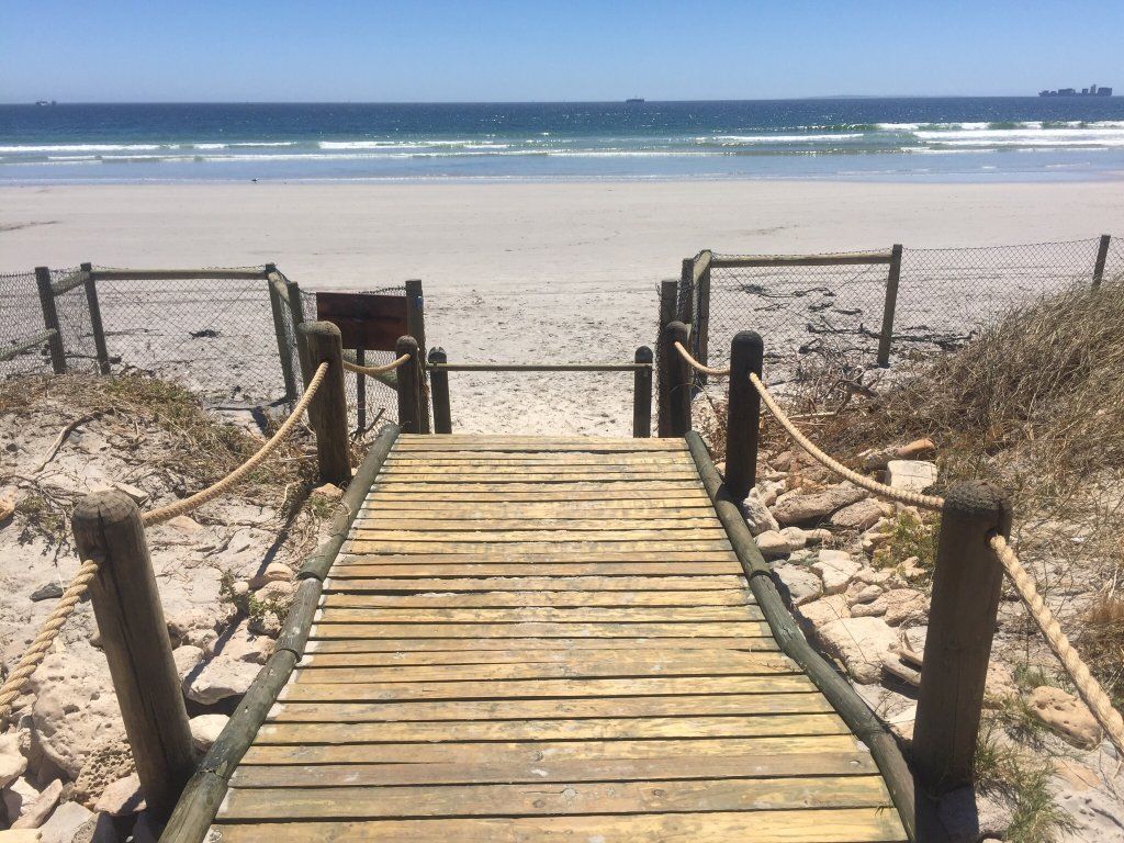 A wooden boardwalk leading to a sandy beach with a fence on either side.