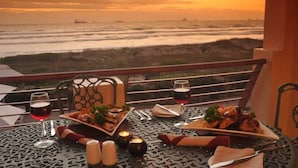 A dining table set with plates of food, glasses of wine, and candles on a balcony overlooking the ocean at sunset. - Leisure Bay (Cape Town)