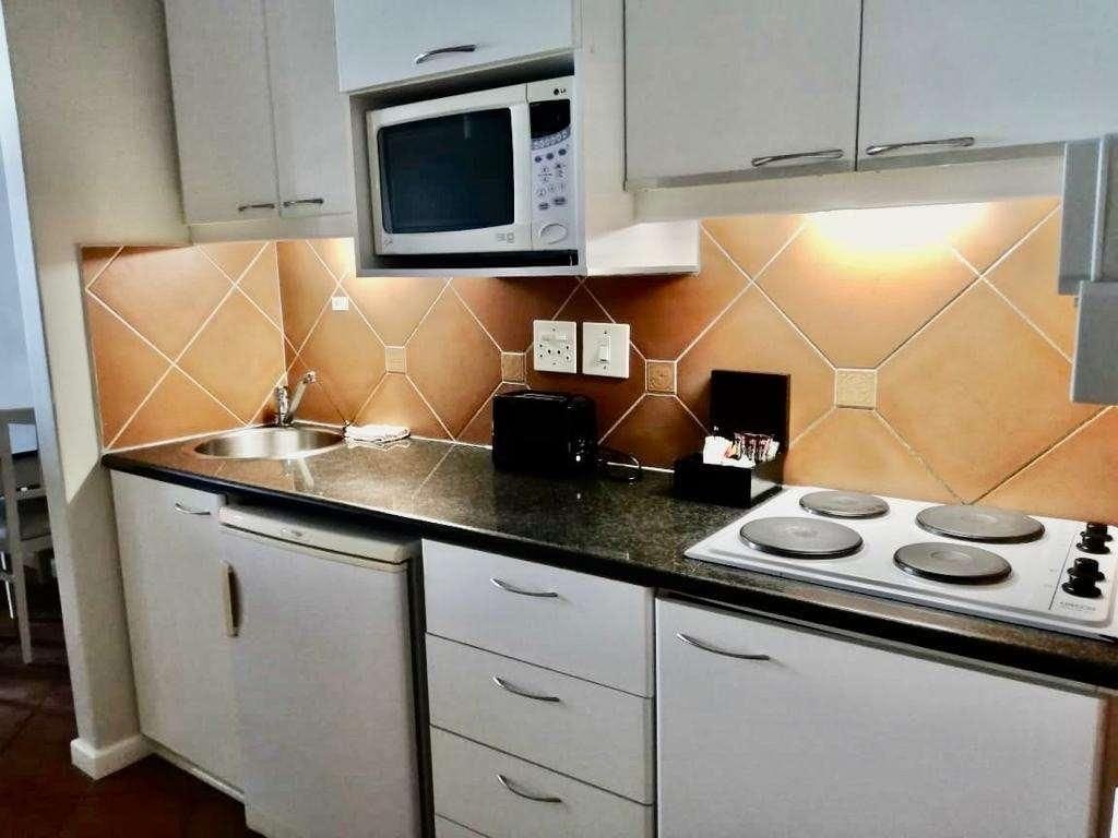 A compact kitchen with a microwave, stove, sink, and white cabinets.