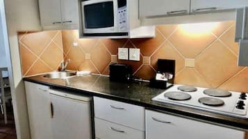 A compact kitchen with a microwave, stove, sink, and white cabinets.