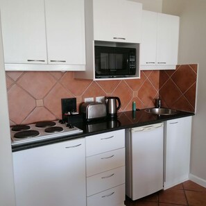 A compact kitchen with white cabinets, a black microwave, a stove, a toaster, a kettle, and a Samsung dishwasher. - Leisure Bay (Cape Town)