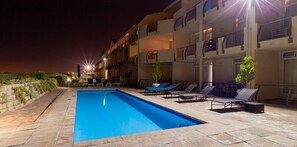 A swimming pool with lounge chairs and a building with balconies.