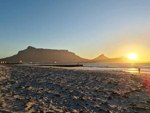 A beach with a pier extending into the water, a mountain in the background, and the sun setting over the horizon. - Leisure Bay (Cape Town)