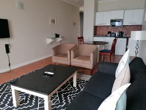 A living room with a black sofa, two patterned armchairs, a coffee table, and a TV mounted on the wall. - Leisure Bay (Cape Town)