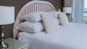 A neatly made bed with white linens and multiple pillows, a bedside lamp, and a view of the sea through curtains. - Leisure Bay (Cape Town)