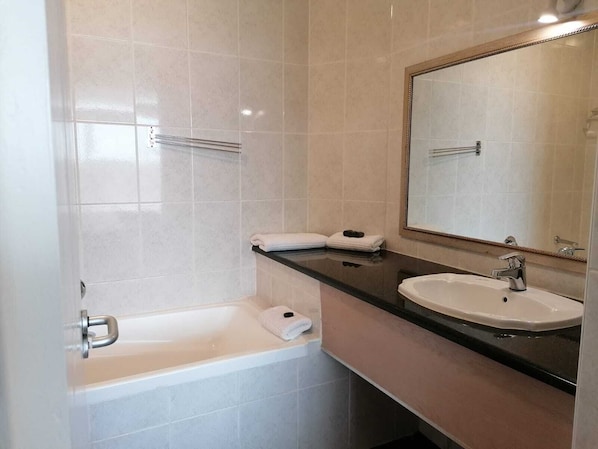 A bathroom with a bathtub, a sink, and a mirror. - Leisure Bay (Cape Town)