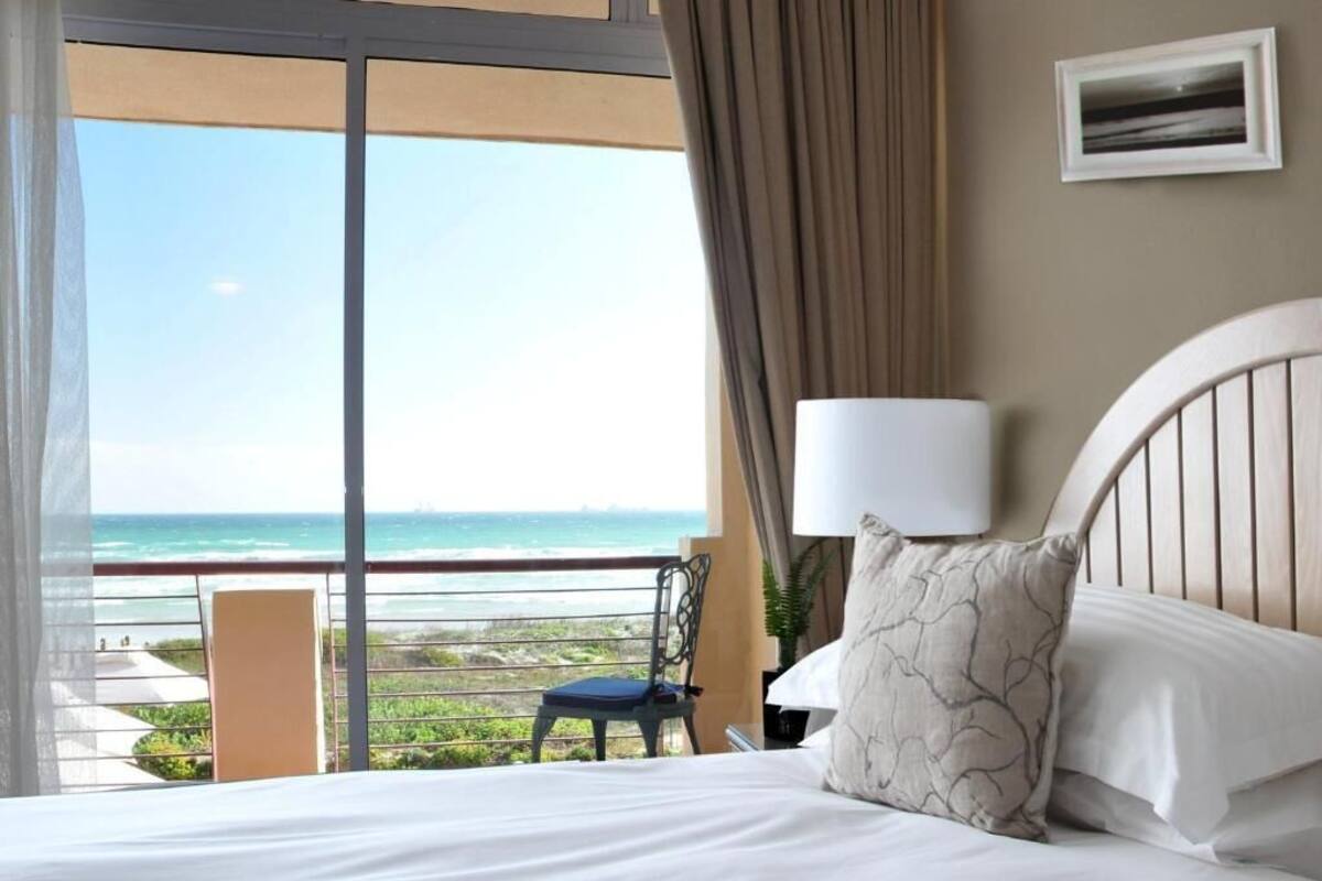 A hotel room with a bed, a chair, a lamp, and a view of the ocean.