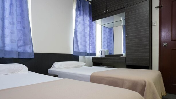A hotel room with two beds, a wooden wardrobe, a mirror, and a door. - Amrise Hotel (SINGAPORE)
