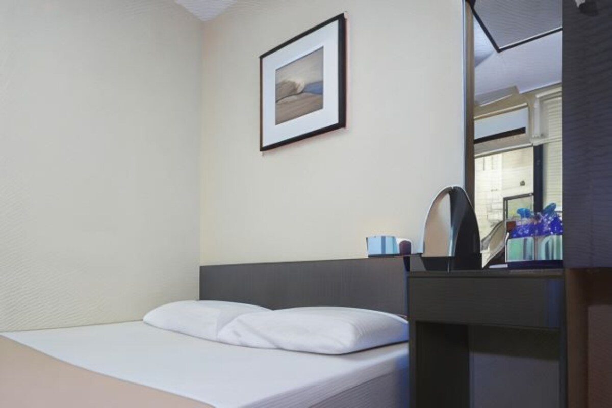 A hotel room with a bed, a framed picture on the wall, a mirror, and a small table with items on it.