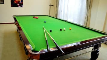 A pool table with balls and cues, a window with curtains, and a wall-mounted clock.