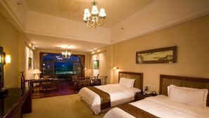 Habitación de hotel con dos camas, un candelabro, un escritorio y vista a la ciudad de noche.