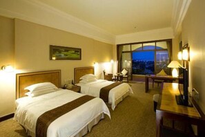 Habitación de hotel con dos camas, un escritorio y un ventanal con vistas.