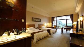 A hotel room with two beds, a desk, and a large window.