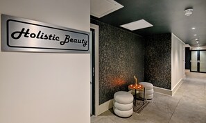 A hallway with a sign reading 'Holistic Beauty,' a wall with a tree pattern, and a small table with candles. - Capetonian Hotel (Cape Town)